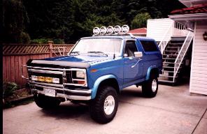 1985 Ford Bronco - A blue 1985 Ford Bronco is parked in a driveway next to a house.