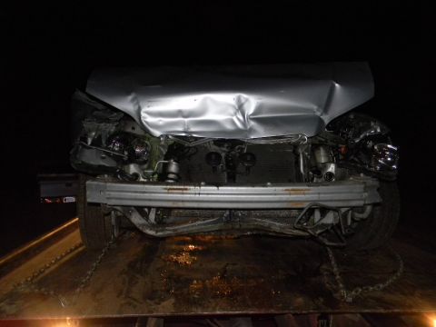 1975 Ford Ranchero - This severely damaged vehicle, likely a pickup truck or car, is being towed, with its front end crumpled and engine exposed.