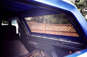 1985 Ford Bronco - View from inside a blue SUV, looking out through the rear window at a backyard scene.