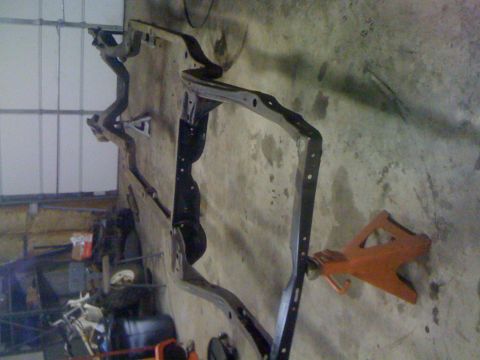 1986 Ford F-150 - A bare vehicle frame is supported by an orange jack stand in a workshop setting.