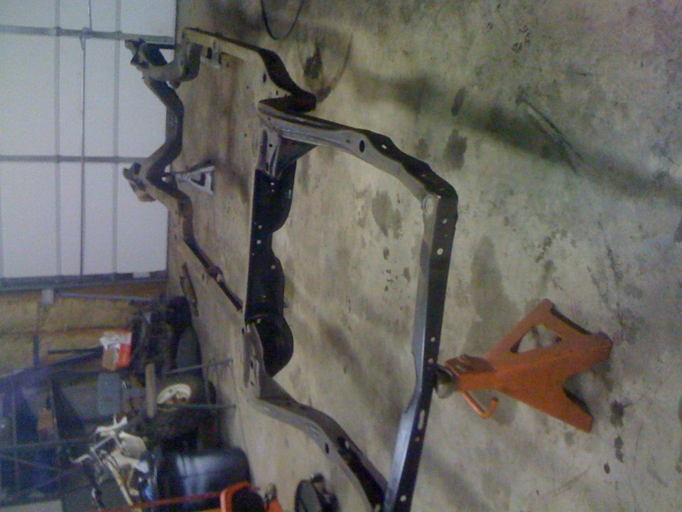 Black metal vehicle frame on an orange jack stand against a concrete wall