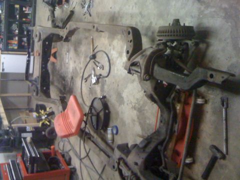 1986 Ford F-150 - Various vehicle parts, including a frame and suspension components, are organized on a workshop floor.