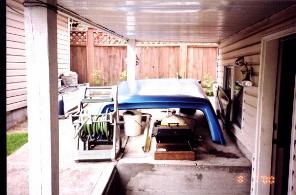 1985 Ford Bronco - A blue soft top is stored under a covered patio next to a hose reel.