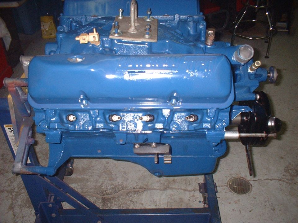 Blue engine block on a blue stand, front view, with spark plugs visible