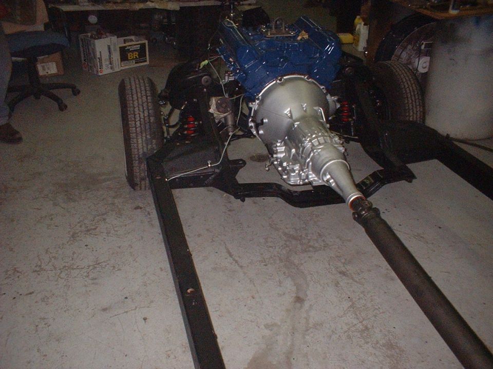 Bare frame with blue V8 engine, silver automatic transmission and driveshaft in a garage