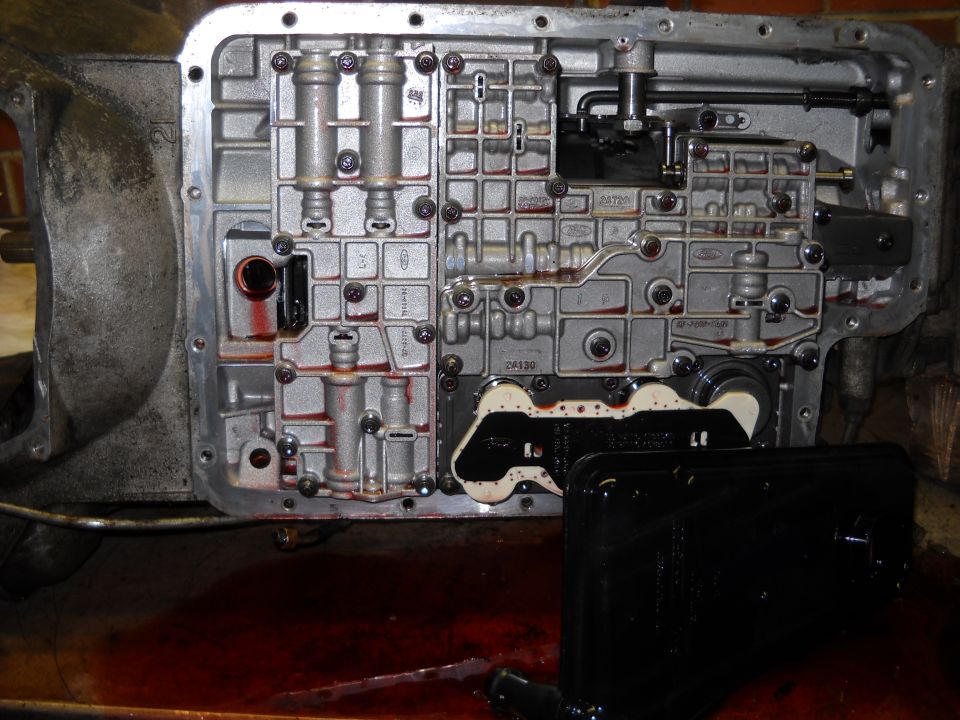 Transmission valve body with solenoids and filter pan removed, showing red fluid