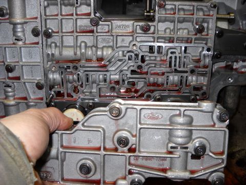 1993 Ford C-150 (Centurion Conversions) - Close-up of a Ford automatic transmission valve body, showing internal passages and a hand interacting with a part.