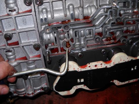 1993 Ford C-150 (Centurion Conversions) - A mechanic's hand uses a tool to manipulate the internal components of an E4OD transmission valve body.