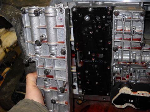 1993 Ford C-150 (Centurion Conversions) - A mechanic's hand is visible near a disassembled automatic transmission valve body, showing internal components and red fluid.