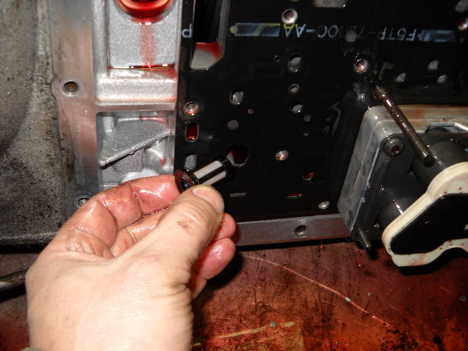 Hand holding a small transmission filter with a black and white mesh element, in front of a transmission valve body