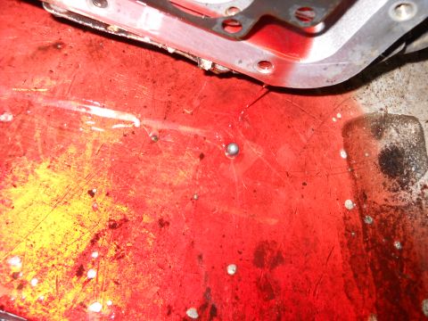 1993 Ford C-150 (Centurion Conversions) - Close-up of a transmission pan showing red fluid, metal debris, and a ball bearing, indicating potential internal wear.