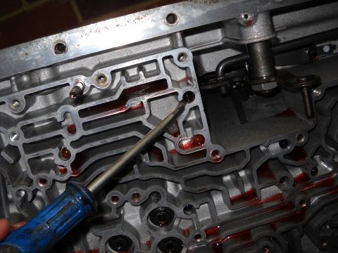 1993 Ford C-150 (Centurion Conversions) - Close-up of an automatic transmission valve body showing internal passages filled with red fluid.