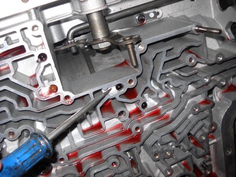 1993 Ford C-150 (Centurion Conversions) - Close-up of an automatic transmission valve body, showing fluid channels and a screwdriver.