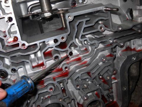 1993 Ford C-150 (Centurion Conversions) - Close-up of an automatic transmission valve body, showing internal passages filled with red fluid, with a tool inserted.