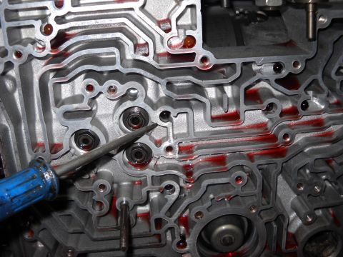 1993 Ford C-150 (Centurion Conversions) - A close-up view of an automatic transmission valve body, showing fluid channels and a tool being used.