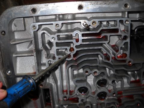 1993 Ford C-150 (Centurion Conversions) - Close-up of an automatic transmission valve body, showing fluid-filled channels and a screwdriver.