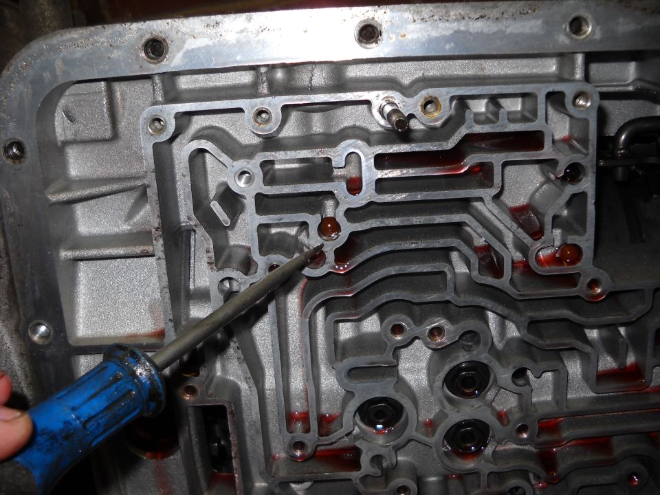 Automatic transmission valve body with red fluid in channels, being probed by a screwdriver