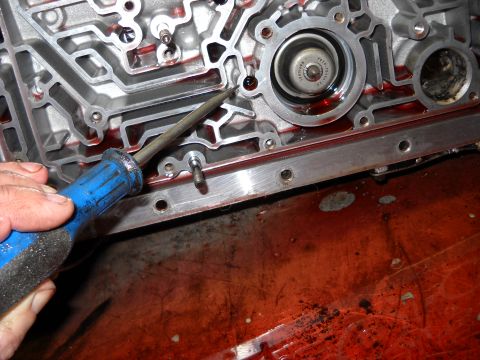 1993 Ford C-150 (Centurion Conversions) - Mechanic uses a screwdriver to work on an automatic transmission valve body, with red fluid present.