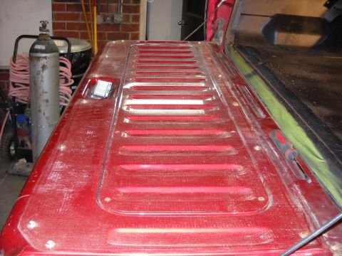 1993 Ford C-150 (Centurion Conversions) - The tailgate of a red truck features a distinctive horizontal vent pattern and a small white tag attached near the latch.