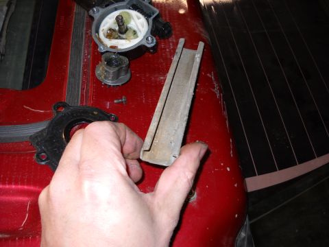 1993 Ford C-150 (Centurion Conversions) - Disassembled water pump parts are laid out on a red surface, with a hand holding a metal channel piece.