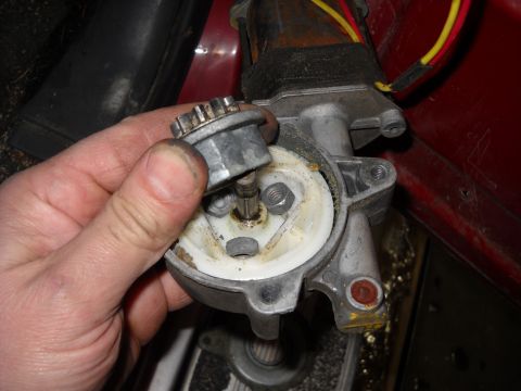 1993 Ford C-150 (Centurion Conversions) - Disassembled power window motor assembly with a hand holding a gear. Red interior trim is visible in the background.