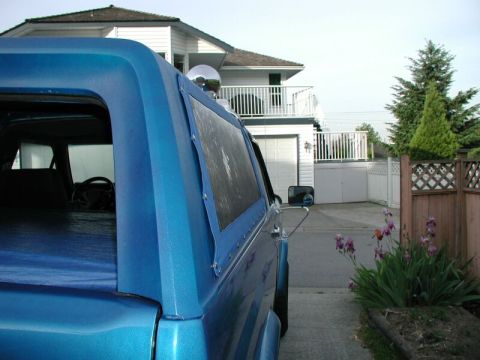 1985 Ford Bronco - Side view of a blue 1985 Ford Bronco a soft top and a chrome side mirror.