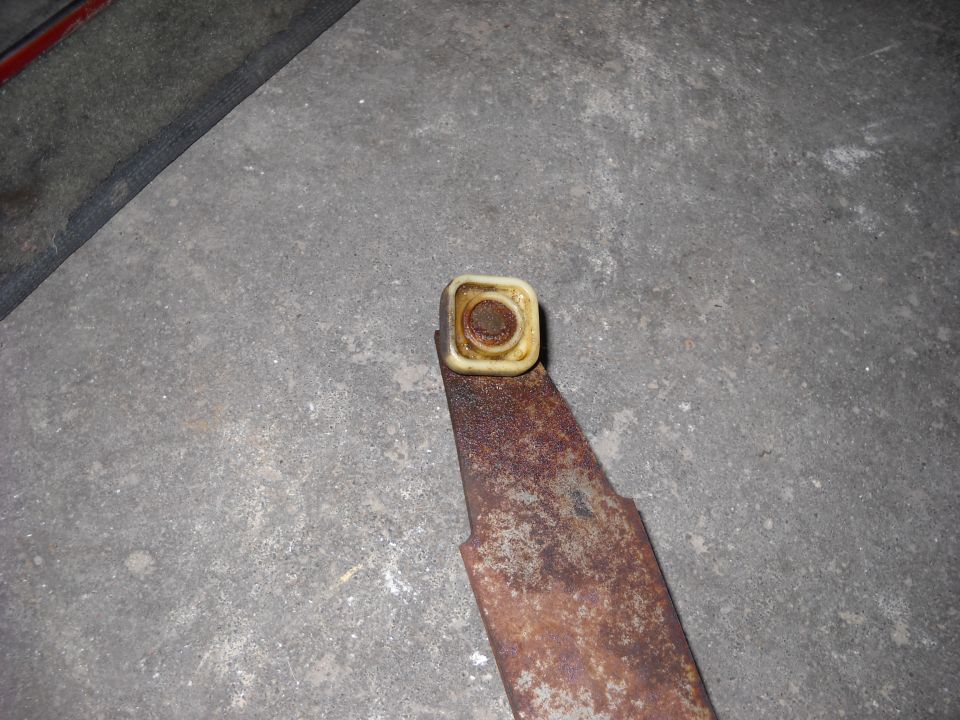 Rusted metal bracket with a square cream-colored plastic cap on a concrete floor