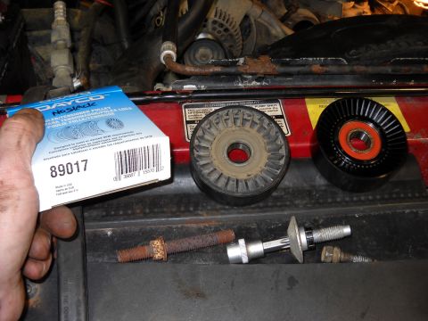 1993 Ford C-150 (Centurion Conversions) - A hand holds a new pulley box near old and new engine pulleys and mounting hardware.