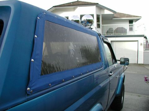 1985 Ford Bronco - The side of a blue SUV is shown with a blue soft top covering the rear section.