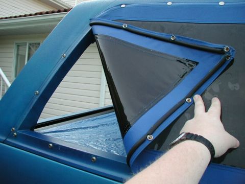 1985 Ford Bronco - A hand adjusts a triangular clear window on a blue soft top, likely for a truck or SUV.