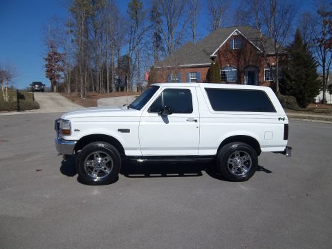 1995 Ford Bronco - A white Ford Bronco is parked on a street in front of a house.