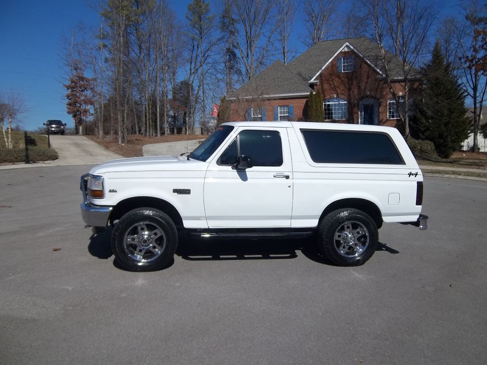 White Ford Bronco parked on asphalt, side view. Chrome wheels, tinted windows