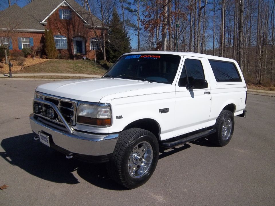 White 1995 Ford Bronco with chrome bull bar and aftermarket wheels parked in front of a house