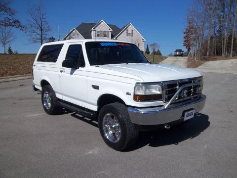 1995 Ford Bronco - A white Ford Bronco is parked in a driveway with houses in the background under a clear blue sky.