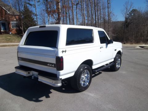 1995 Ford Bronco - A white 1992 Ford Bronco is parked outdoors on a paved surface, with trees and a house in the background.