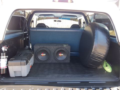 1995 Ford Bronco - The cargo area of the vehicle is equipped with a dual subwoofer box, a toolbox, and a spare tire cover.