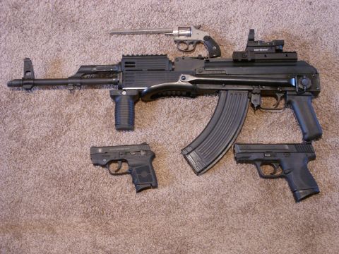 1978 Ford Mustang II - A collection of firearms, including an assault rifle and handguns, are displayed on a brown carpet.