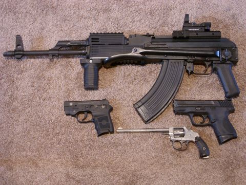 1978 Ford Mustang II - A collection of firearms, an assault rifle and several handguns, laid out on a carpeted floor.
