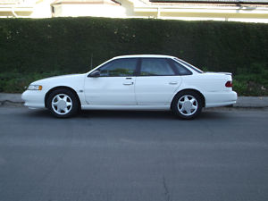 1993 Ford Taurus - Side profile of a white 1993 Ford Taurus sedan parked on a residential street.