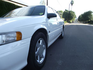 1993 Ford Taurus - A white 1993 Ford Taurus is seen from a low angle, capturing its side profile and front wheel.