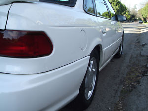 1993 Ford Taurus - The rear of a white 1993 Ford Taurus sedan is shown from a low angle, highlighting the taillight and rear wheel.