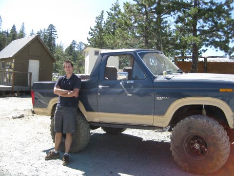 1986 Ford Bronco - A man stands next to a blue Ford Bronco with tan trim and large tires.