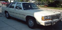 1997 Ford Crown Victoria - A cream-colored sedan is parked on the street, with another vehicle in the background.