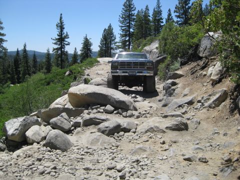 1986 Ford Bronco - A Ford F-Series truck navigates a challenging, rocky off-road trail in a mountainous, wooded area.