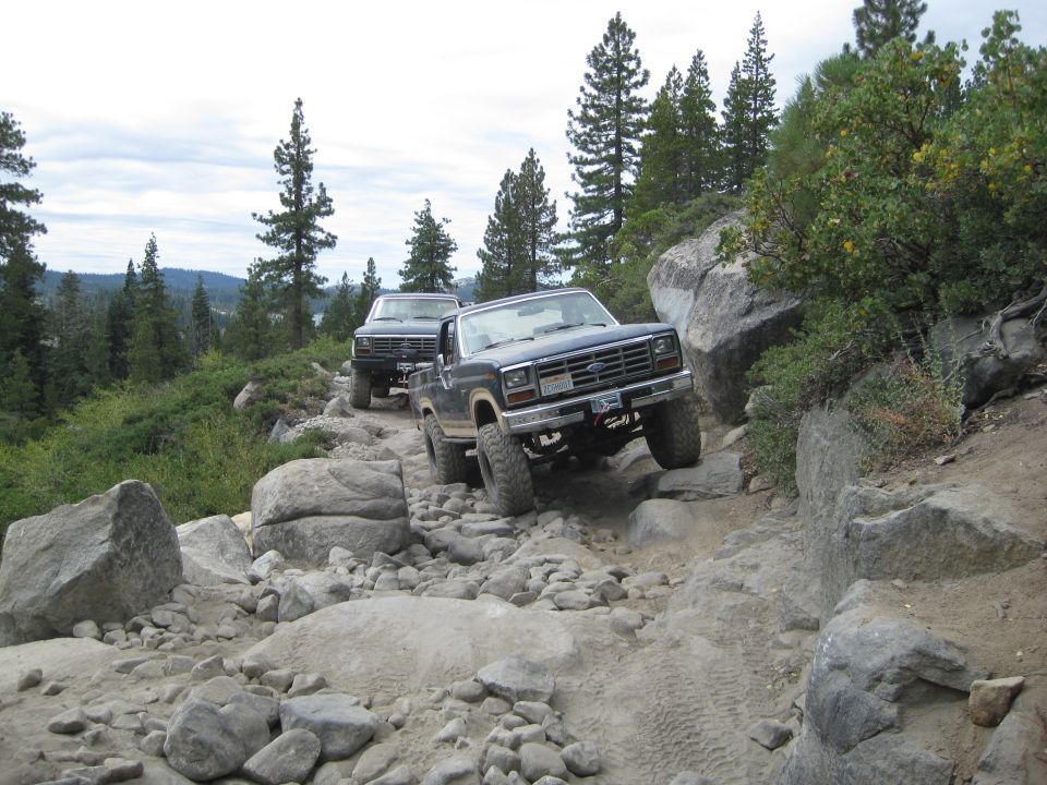 Dark blue Ford Bronco navigating a rocky trail, front-right wheel elevated
