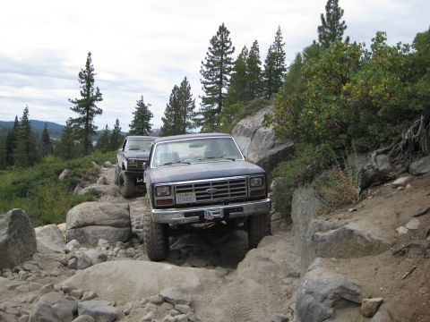 1986 Ford Bronco - Two SUVs tackle a challenging rocky off-road trail, with the lead vehicle appearing to be a 1980s Ford Bronco.