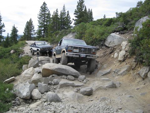 1986 Ford Bronco - Two trucks tackle a challenging rocky trail in a mountainous, wooded area.