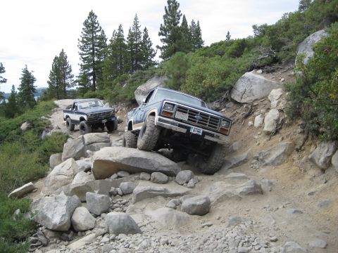 1986 Ford Bronco - Two Ford pickup trucks tackle a challenging rocky trail, demonstrating their off-road capabilities on a steep incline.