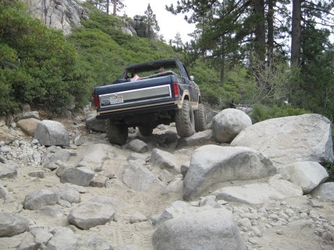 1986 Ford Bronco - A Ford Bronco navigates a rocky off-road trail in a mountainous, wooded area.