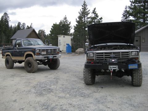 1986 Ford Bronco - Two modified Ford trucks are parked outdoors on a cloudy day.